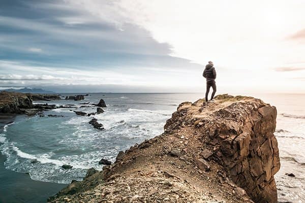 strong individual standing on cliffside overlooking ocean